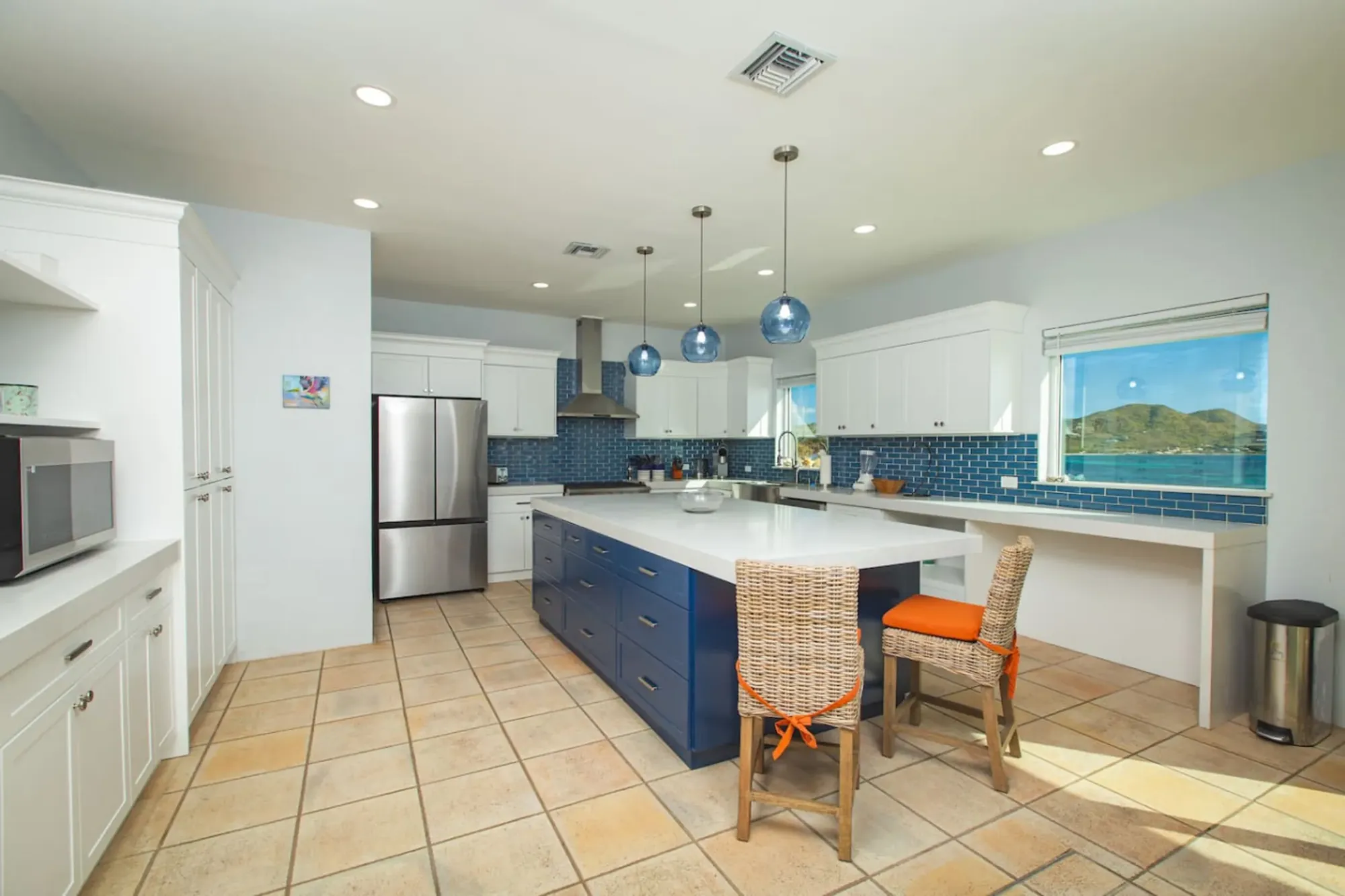 The chef's kitchen: a blue island, a full range and a sea-view window, with a second refrigerator in the cottage for the market haul.
