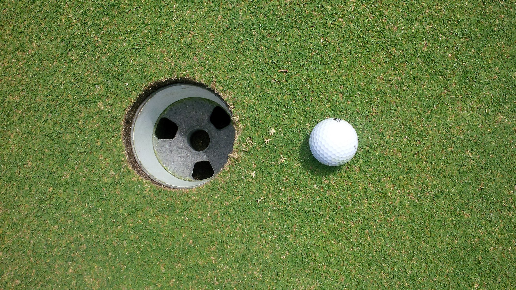 A golf ball beside the cup on a putting green